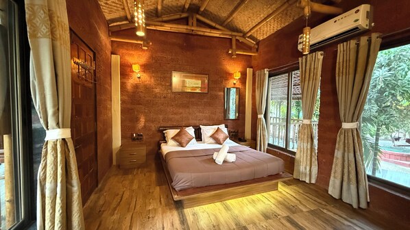 A room with a wooden floor, a bed with pillows, a wall-mounted air conditioner, and a window with curtains.