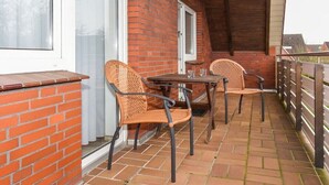 Een overdekt terras met een bakstenen muur, twee rieten stoelen, een tafel en een raam.