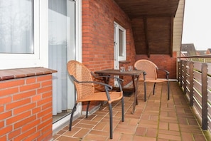 A covered patio with a brick wall, two wicker chairs, a table, and a window. - holiday apartment "Seehund 1" (Esens-Bensersiel)