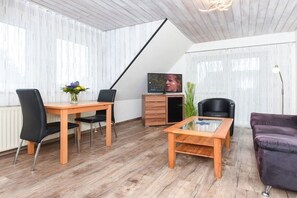 A modern living room with a wooden dining table, black chairs, a glass coffee table, a television, and a purple sofa. - holiday apartment "Seehund 1" (Esens-Bensersiel)