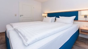 Een hotelkamer met een bed, nachtkastje, lamp en een deur.