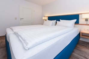 A hotel room with a bed, a nightstand, a lamp, and a door. - holiday apartment "Seehund 1" (Esens-Bensersiel)