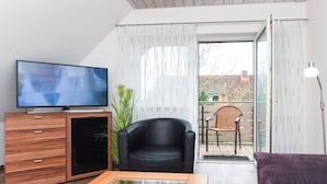 Een moderne woonkamer met een flatscreentelevisie, houten meubels, een zwarte leren fauteuil en een paarse bank.