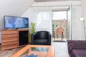 A modern living room with a flat-screen TV, wooden furniture, a black leather chair, and a purple sofa. - holiday apartment "Seehund 1" (Esens-Bensersiel)