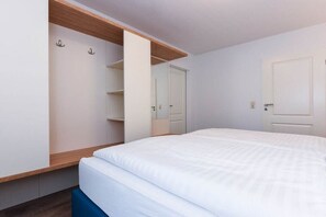 Une chambre à coucher avec un lit, une armoire dont les portes sont ouvertes, et une porte donnant sur une autre pièce.