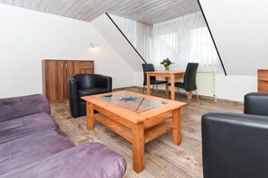 Une pièce de style « loft », avec un plancher en bois, une table basse au plateau en verre, un canapé violet, un fauteuil en cuir noir et une table à manger avec des chaises.