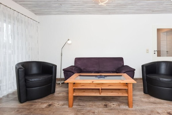 A room with a wooden coffee table, two black leather chairs, a purple sofa, and a floor lamp. - holiday apartment "Seehund 1" (Esens-Bensersiel)
