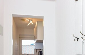 A hallway with a white door, a hanging light fixture, and a view into a room with a window. - holiday apartment "Seehund 1" (Esens-Bensersiel)