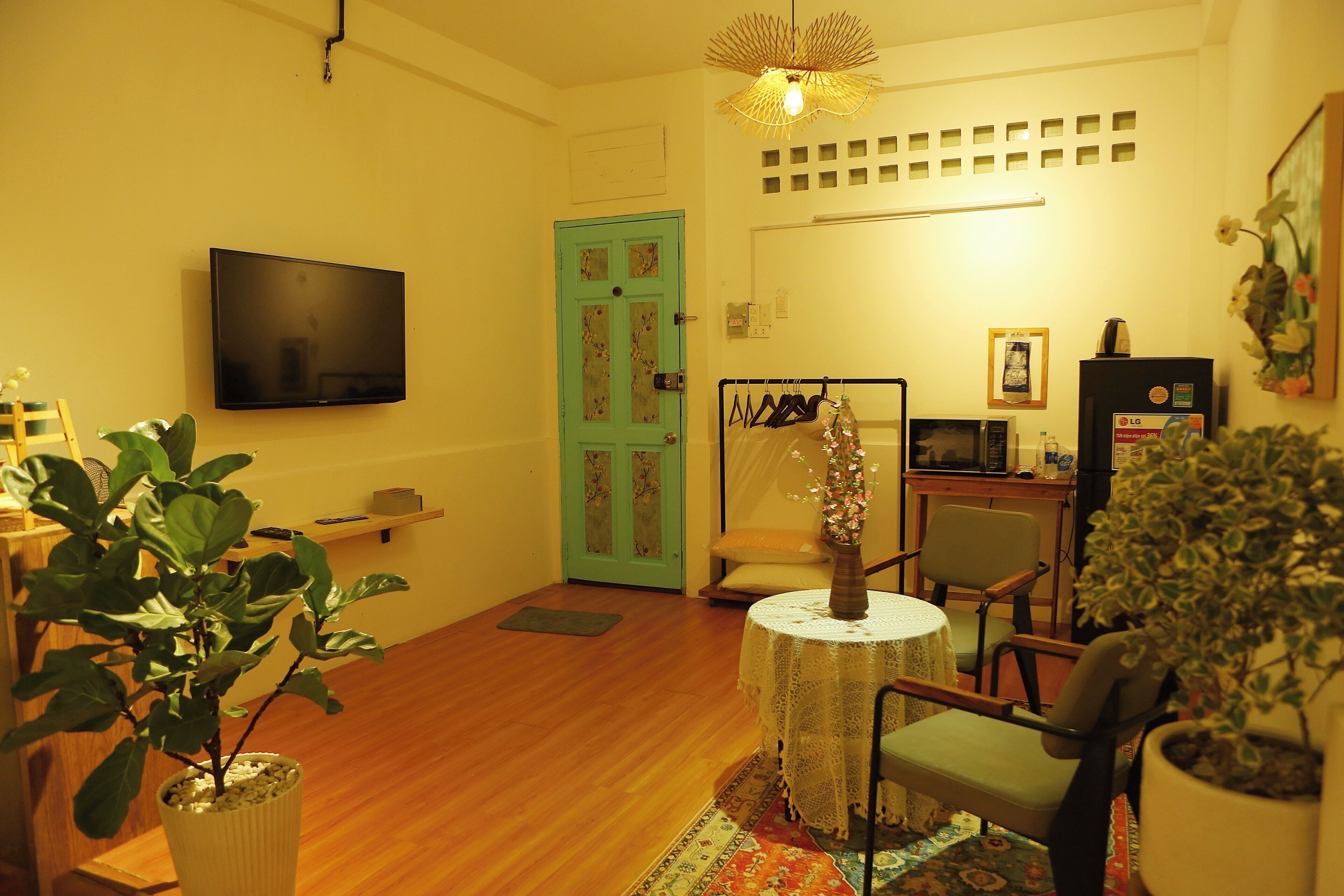 A living room with a flat-screen TV, a green door, a table with a vase, and a chair.