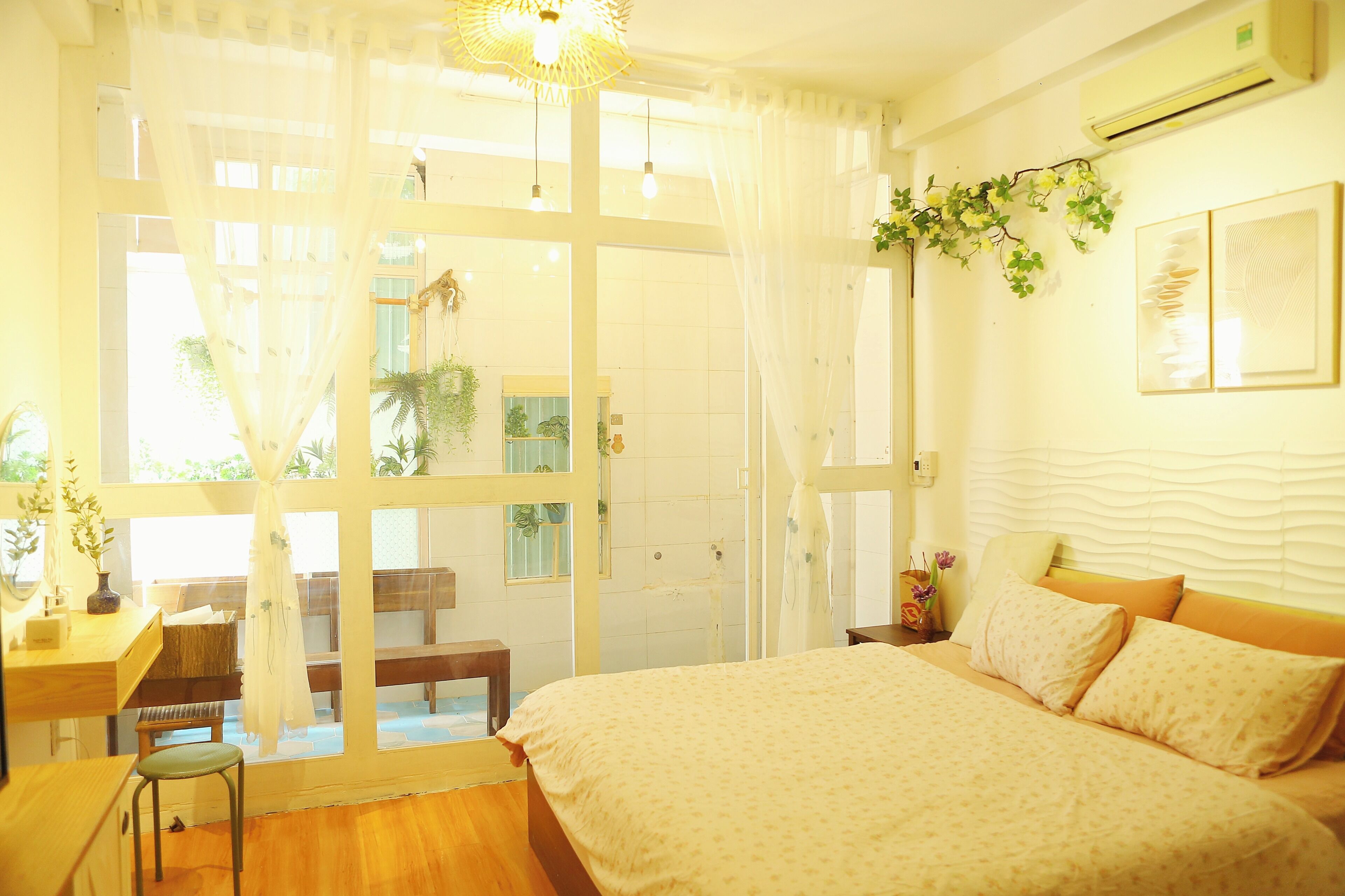A bedroom with a large bed, a desk, and a chair. There is a window with curtains and a view of the outside.