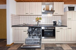 Eine moderne Küche mit hellen Holzschränken, einem Edelstahl-Geschirrspüler, einem Backofen und einer Kaffeemaschine.