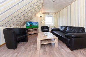 Ein Loft-Wohnzimmer mit Holzboden, einer schwarzen Ledersofa, einem schwarzen Sessel, einem Holztisch und einem Fernseher auf einem Holzständer.