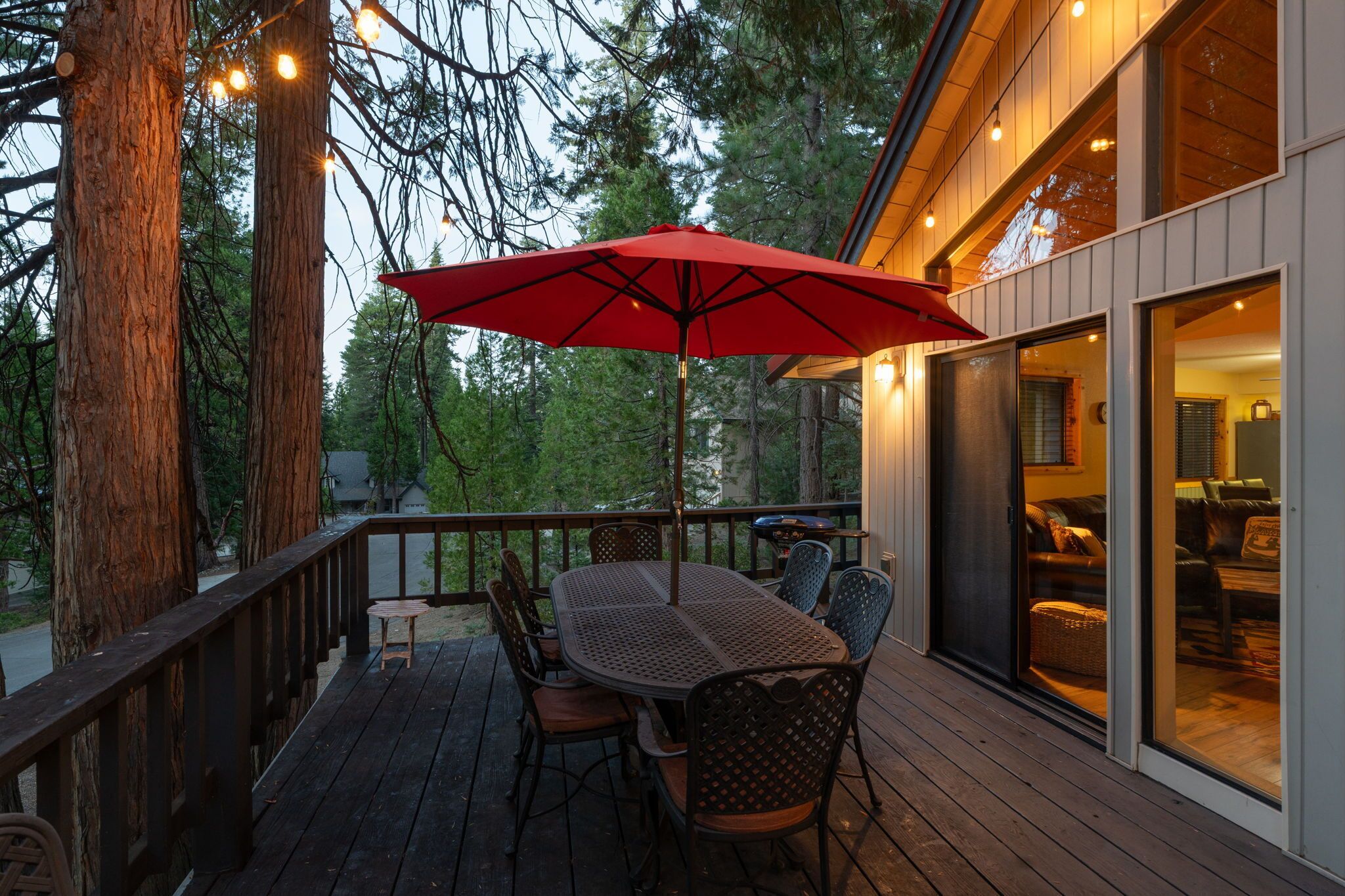 A wooden deck with a table and chairs, a red umbrella, and a glass door leading to an interior space.