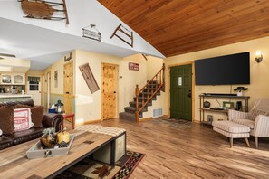 A cozy living room with a wooden staircase, a television, and a kitchen in the background. - Your cozy home away from home in Shaver Lake! (Shaver Lake)