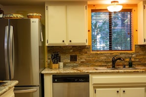 A kitchen with a built-in refrigerator, a stone backsplash, a window with blinds, and a countertop with a knife block. - Your cozy home away from home in Shaver Lake! (Shaver Lake)