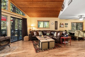 Un salon chaleureux avec un plafond en bois, un canapé en cuir, une table basse et un coin repas comprenant des chaises et une table.