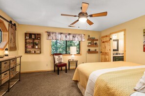 Ein Schlafzimmer mit einem Bett, einem Schreibtisch, einem Stuhl, einem Deckenventilator und einem Fenster mit Jalousien.