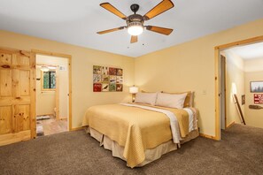 A bedroom with a bed, a ceiling fan, a wall with artwork, and a door leading to another room. - Your cozy home away from home in Shaver Lake! (Shaver Lake)
