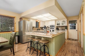 A kitchen with a central island, bar stools, a refrigerator, and a dining table. - Your cozy home away from home in Shaver Lake! (Shaver Lake)