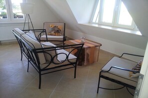 Een kamer met schuine wanden, een bank, een stoel, een klein tafeltje en een raam met uitzicht.
