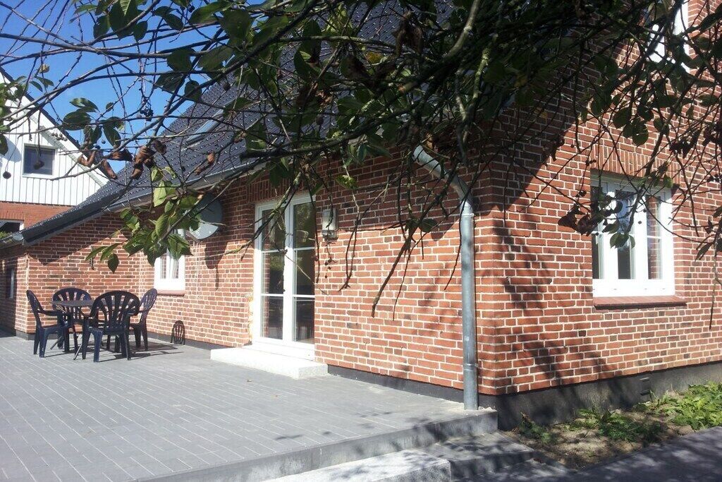 Un edificio de ladrillo con un patio, mobiliario exterior y un árbol en primer plano.