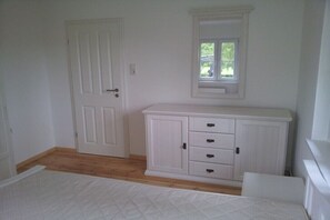 Ein Zimmer mit Tür, Schrank mit Schubladen, Fenster und Bett.