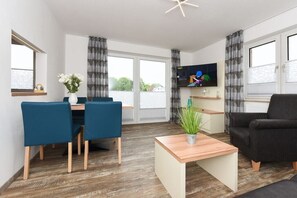 Ein modernes Wohnzimmer mit Essbereich, einem an der Wand befestigten Flachbildfernseher und einem großen Fenster mit Vorhängen.