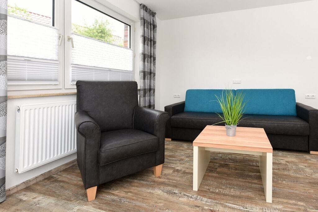 Ein Wohnzimmer mit einem schwarzen Ledersessel, einem blauen Sofa und einem Couchtisch aus Holz mit einer Pflanze.