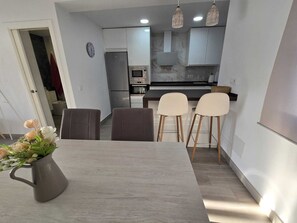 A modern kitchen with stainless steel appliances, a dining area with a grey table and two chairs, and a vase with flowers on the table. - Vrbo Property (Vejer de la Frontera)