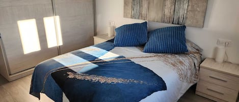 Quarto moderno com cama grande, mesa de cabeceira, luminária na parede e janela com persianas.