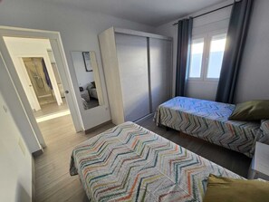 A bedroom with two single beds, a wardrobe, a mirror, and a window with curtains. - Vrbo Property (Vejer de la Frontera)