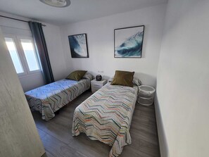 A small, well-lit room with two single beds, a nightstand, and a window with curtains. - Buenavista Vejer Apartment (Vejer de la Frontera)