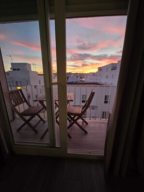 A balcony with two wooden chairs and a table, overlooking a cityscape during sunset. - Buenavista Vejer Apartment (Vejer de la Frontera)