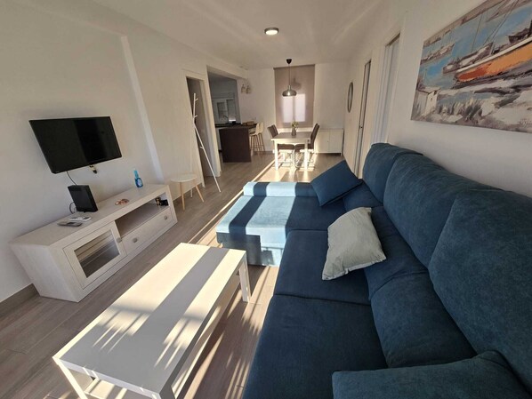A modern living room with a sofa, TV, and a dining area in the background. - Vrbo Property (Vejer de la Frontera)