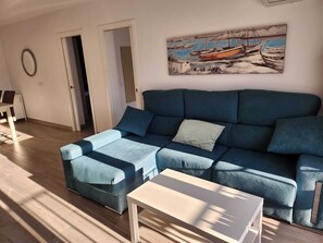 A modern living room with a blue sofa, a white coffee table, and a painting of boats on the wall. - Buenavista Vejer Apartment (Vejer de la Frontera)