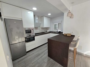 A modern kitchen with white cabinetry, a built-in oven, a microwave, and a dark island counter. - Buenavista Vejer Apartment (Vejer de la Frontera)