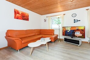 A living room with a sectional sofa, a flat-screen TV, and a painting on the wall. - Holiday apartments "Flut" (Esens-Bensersiel)