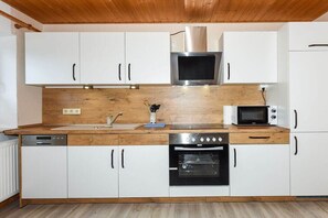 Una cuina compacta amb armaris blancs, microones d'acer inoxidable, forn integrat i rentaplats.