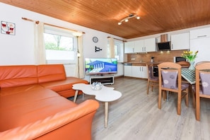 A modern living room with a sofa, a dining table with chairs, a television, and a kitchen area with cabinets and appliances. - Holiday apartments "Flut" (Esens-Bensersiel)