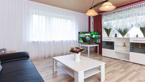 Ett modernt vardagsrum med en soffa, ett vitt soffbord med en vas med blommor, en tv på ett stativ och ett dekorativt skåp.
