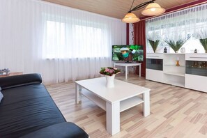 Una sala de estar moderna con un sofá, una mesa de centro blanca con un florero y un televisor sobre un mueble bajo, además de un aparador decorativo.