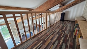 A room with a sloped ceiling, wooden beams, a patterned floor, a sofa, and a bookshelf. - The Malécot Vacation Rental: A 5-person vacation rental in the countryside (Coulon)