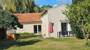 A stone house with a tiled roof, a patio with chairs, and a red umbrella. - Vrbo Property (Coulon)