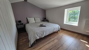 A bedroom with a bed, nightstands, a window, and a view of greenery outside. - The Malécot Vacation Rental: A 5-person vacation rental in the countryside (Coulon)