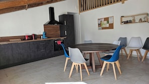 A modern kitchen with dark cabinetry, a built-in stove, and a dining area with a round table and blue chairs. - The Malécot Vacation Rental: A 5-person vacation rental in the countryside (Coulon)