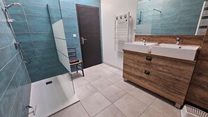 A modern bathroom with a shower, a wooden vanity with a mirror, and a chair. - Vrbo Property (Coulon)