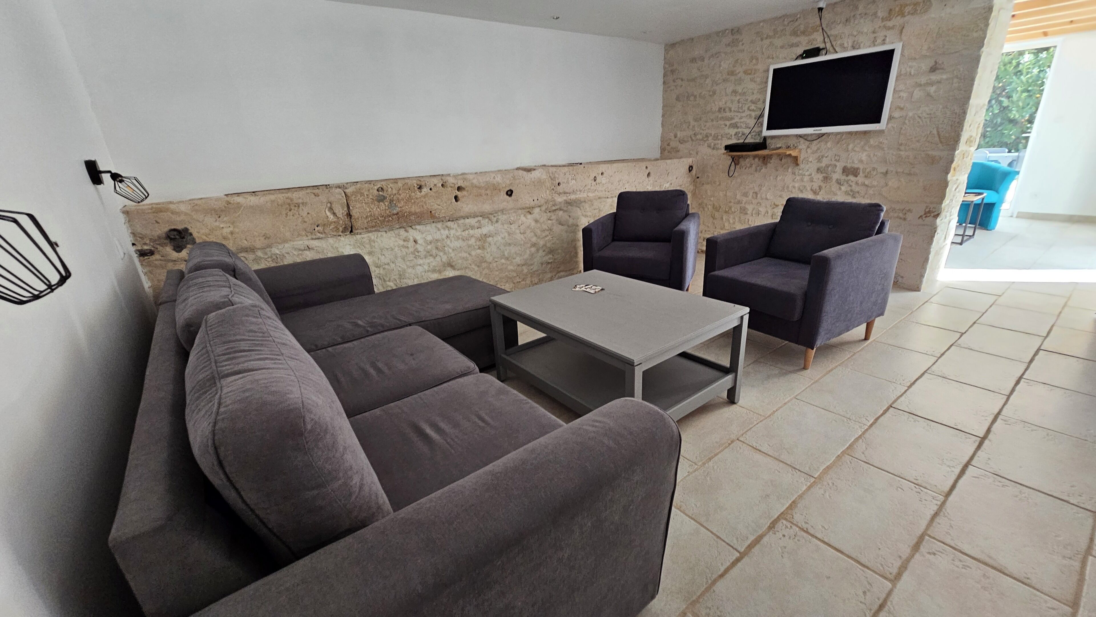 A modern living room with a sectional sofa, two armchairs, a coffee table, and a flat-screen TV mounted on a stone wall.