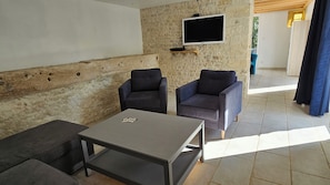 A furnished living area with a sofa, two armchairs, a coffee table, and a flat-screen TV mounted on a textured wall. - The Malécot Vacation Rental: A 5-person vacation rental in the countryside (Coulon)