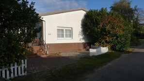 Une maison de plain-pied avec une porte d’entrée, un petit porche et une clôture blanche en bois.
