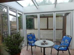 Ein Wintergarten mit Glastür, zwei blaue Stühle mit Blumenmuster, ein kleiner runder Tisch und ein Blumentopf.